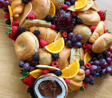 Load image into Gallery viewer, Assorted pastries and fruits arranged in a decorative pattern on a wooden surface.